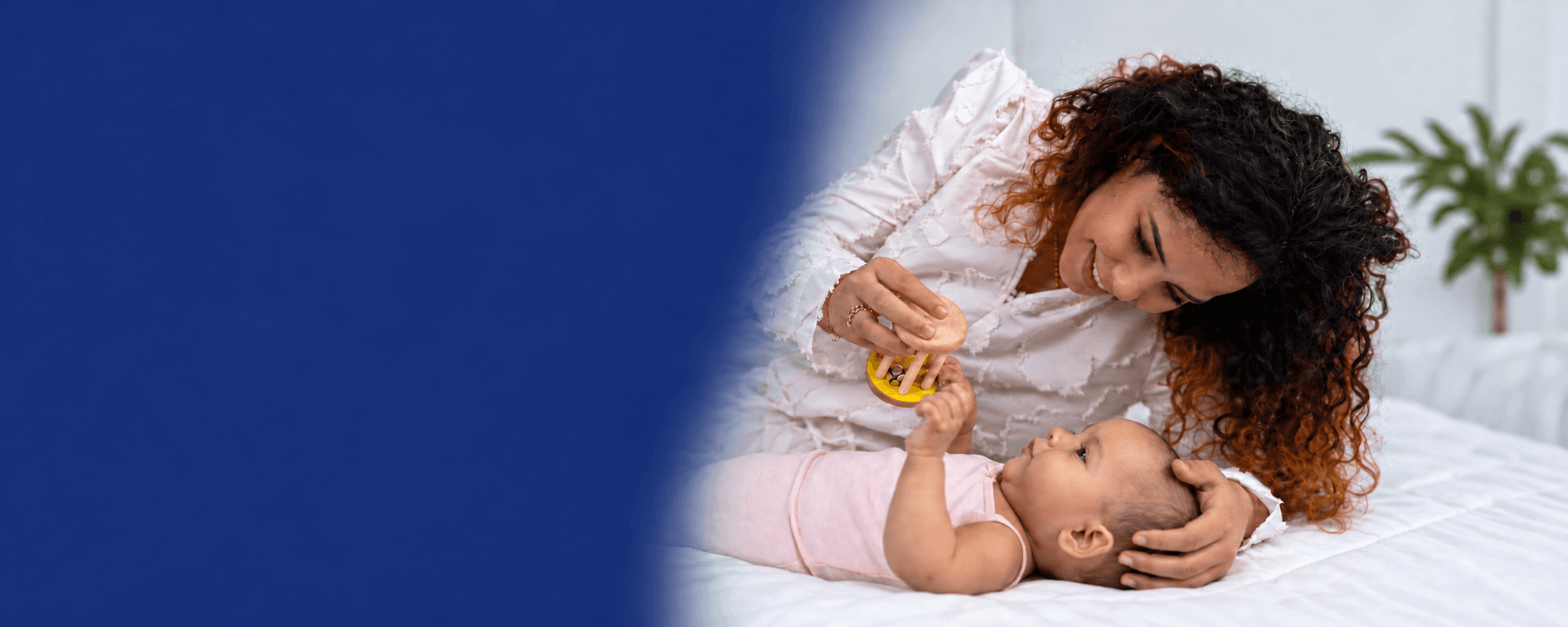 A mother holds a wooden rattle above her newborn, who reaches up for it.